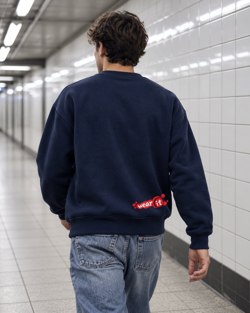 Homme de dos dans un couloir de métro, en sweat col rond bleu marine Wear It, petit logo rouge en bas du dos